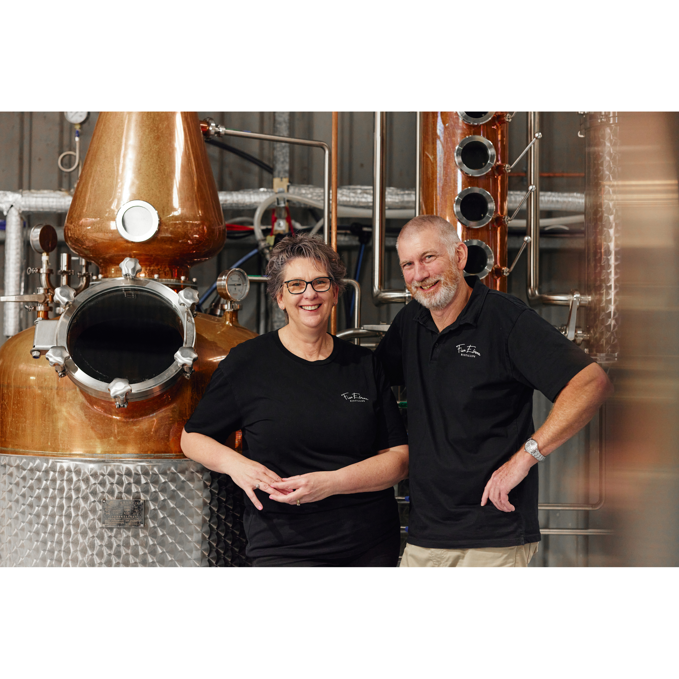 Distillery owners Wayne and Annette standing in front of copper still smiling